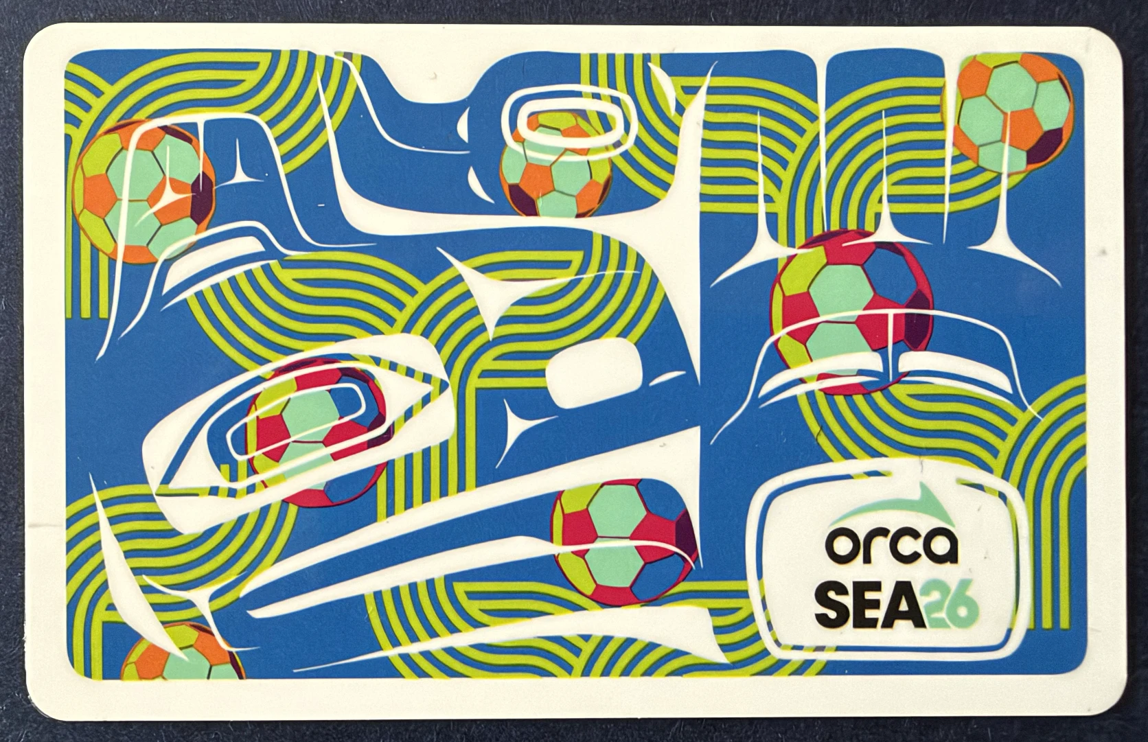 Blue ORCA SEA26 transit card decorated with colorful soccer balls and curved lines